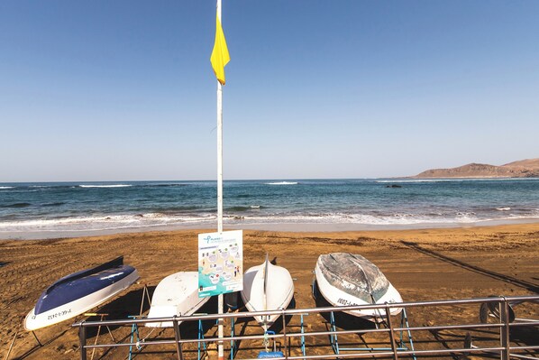 A beach with three surfboards and a signboard.