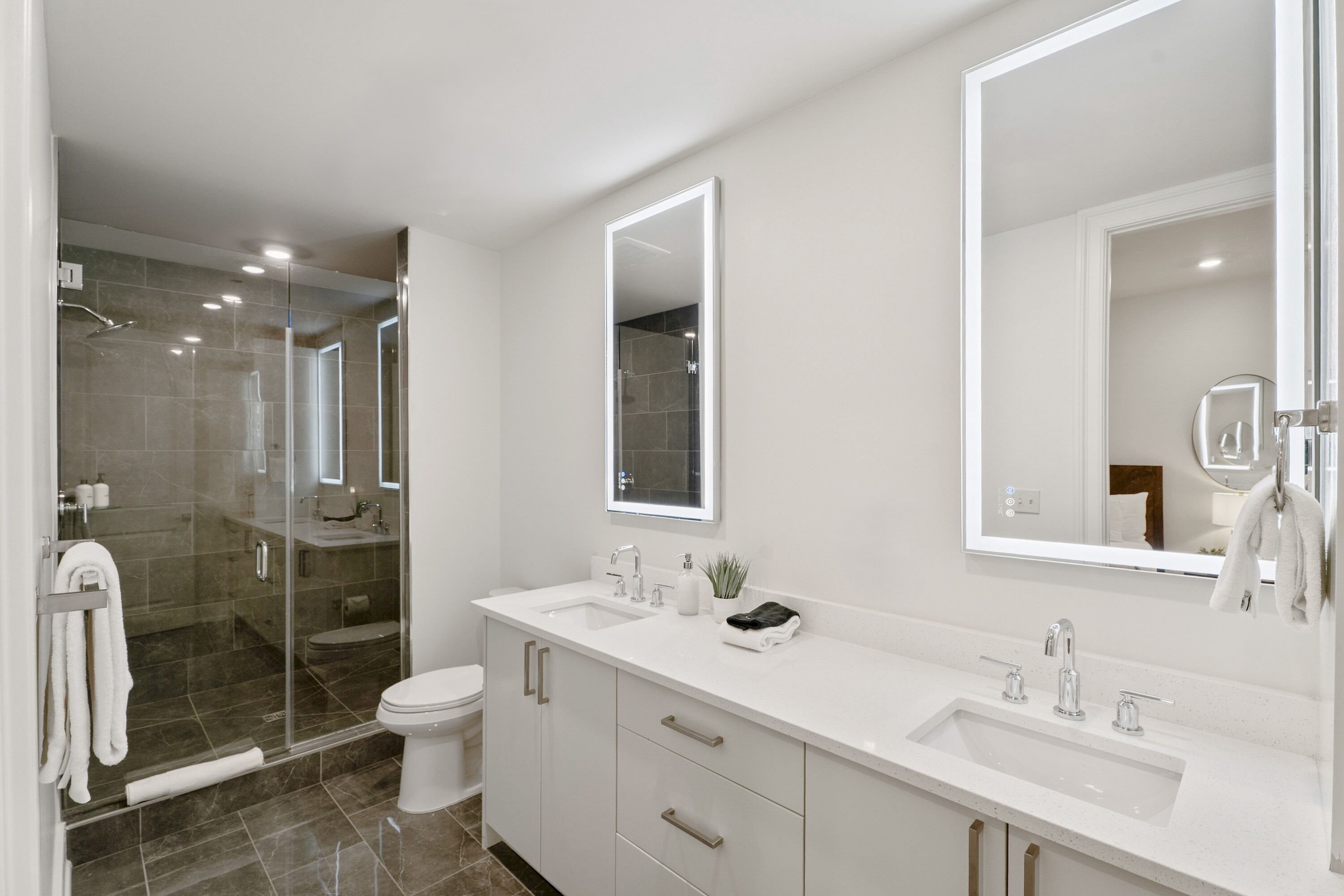 Un baño moderno con ducha de mampara de vidrio, lavamanos blanco y un espejo grande.