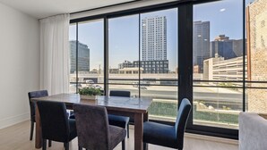 A modern room with a large window, a dining table, and four chairs. - The Theodore 2BD/2B - All King Bedrooms (New Orleans)