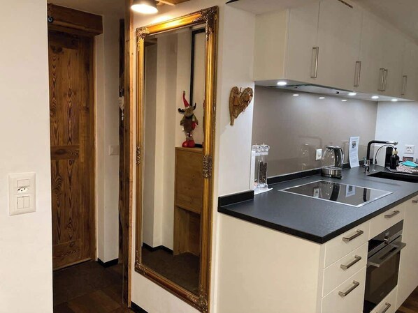 A modern kitchen with a black countertop, white cabinets, and a gold-framed mirror.