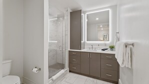 Une salle de bain moderne avec une douche à parois de verre, des toilettes, un lavabo avec un miroir et un meuble-lavabo avec des tiroirs.