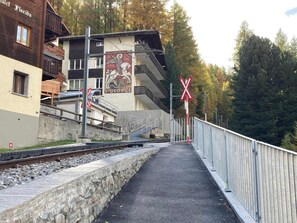 A railway crossing with a pedestrian path, a building with a mural, and a forested background.