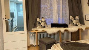 A bedroom with a bed, a dresser, a mirror, a radiator, and a window with curtains. - Cozy Zermatt Studio: Terrace, Village Views (Zermatt)