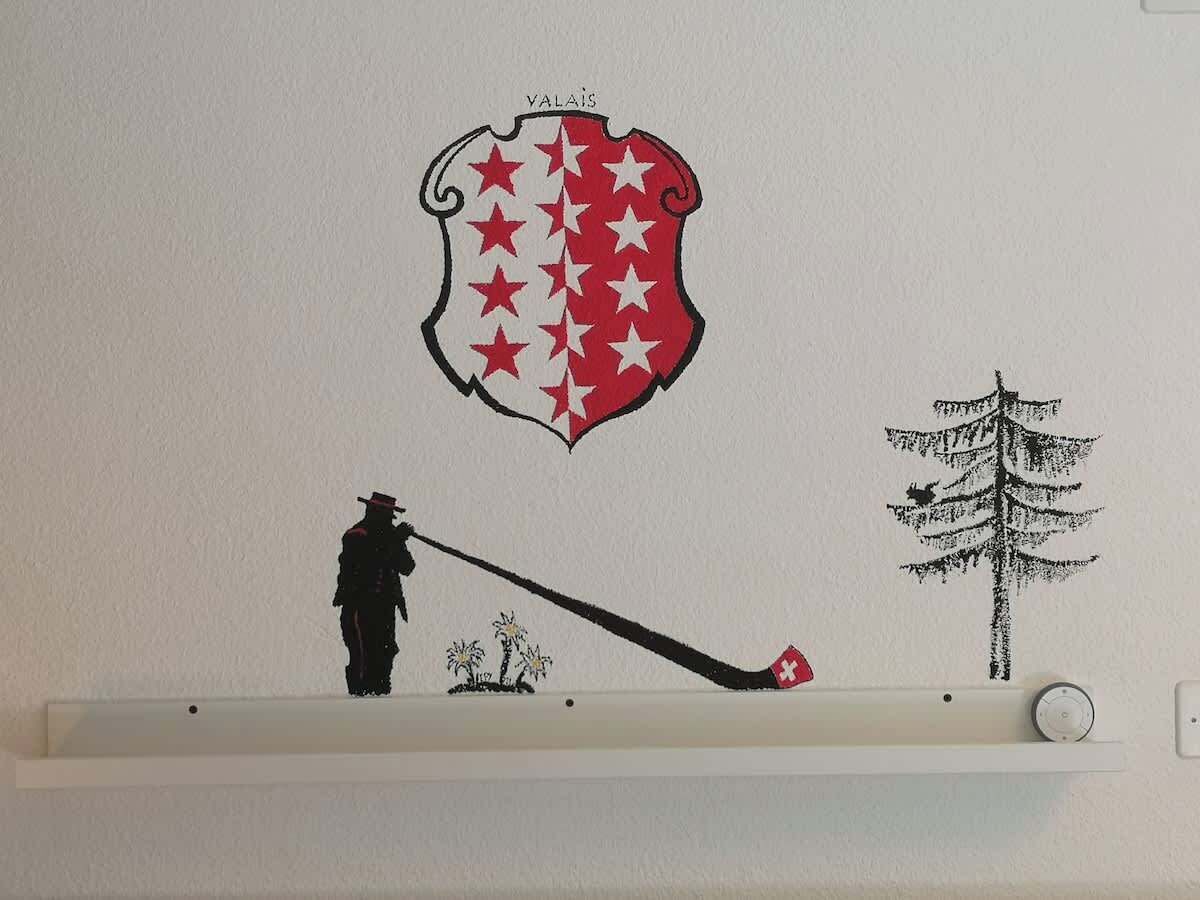 A wall with a shelf displaying a silhouette of a person fishing, a tree, and a shield with stars.