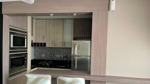 Una cocina moderna con electrodomésticos integrados, salpicadero de azulejos y dos taburetes de bar.