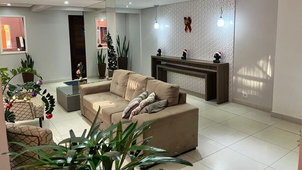 Una sala de estar moderna con un sofá color beige, una mesa de centro y una chimenea. Se ven plantas en macetas y un árbol de Navidad al fondo.