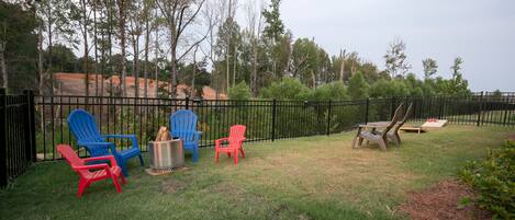 A backyard with a black metal fence, several Adirondack chairs in red and blue, a picnic table, and a small fire pit.