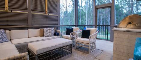 A covered outdoor seating area with a sofa, chairs, and a grill.