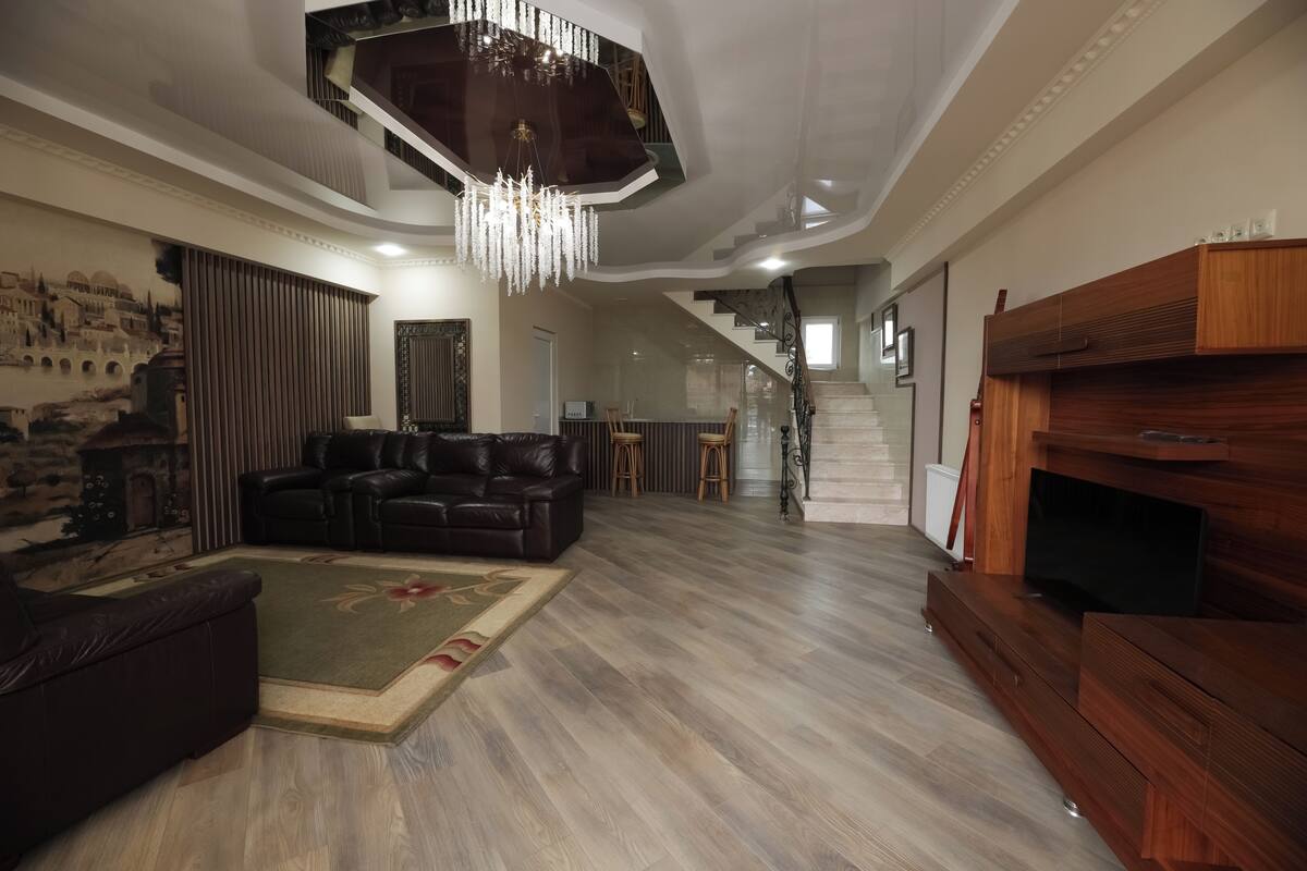 Ein geräumiges Wohnzimmer mit einer großen Holz-TV-Konsole, einem Ledersofa und einer Chandelier.
