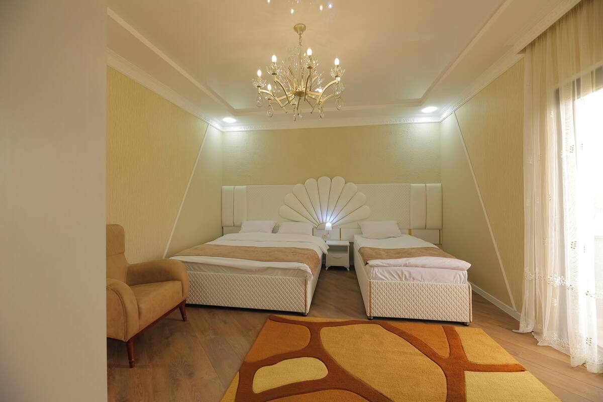 Ein Schlafzimmer mit zwei Betten, einem Sessel, einer Kronleuchter und einem großen Fenster mit Vorhängen.