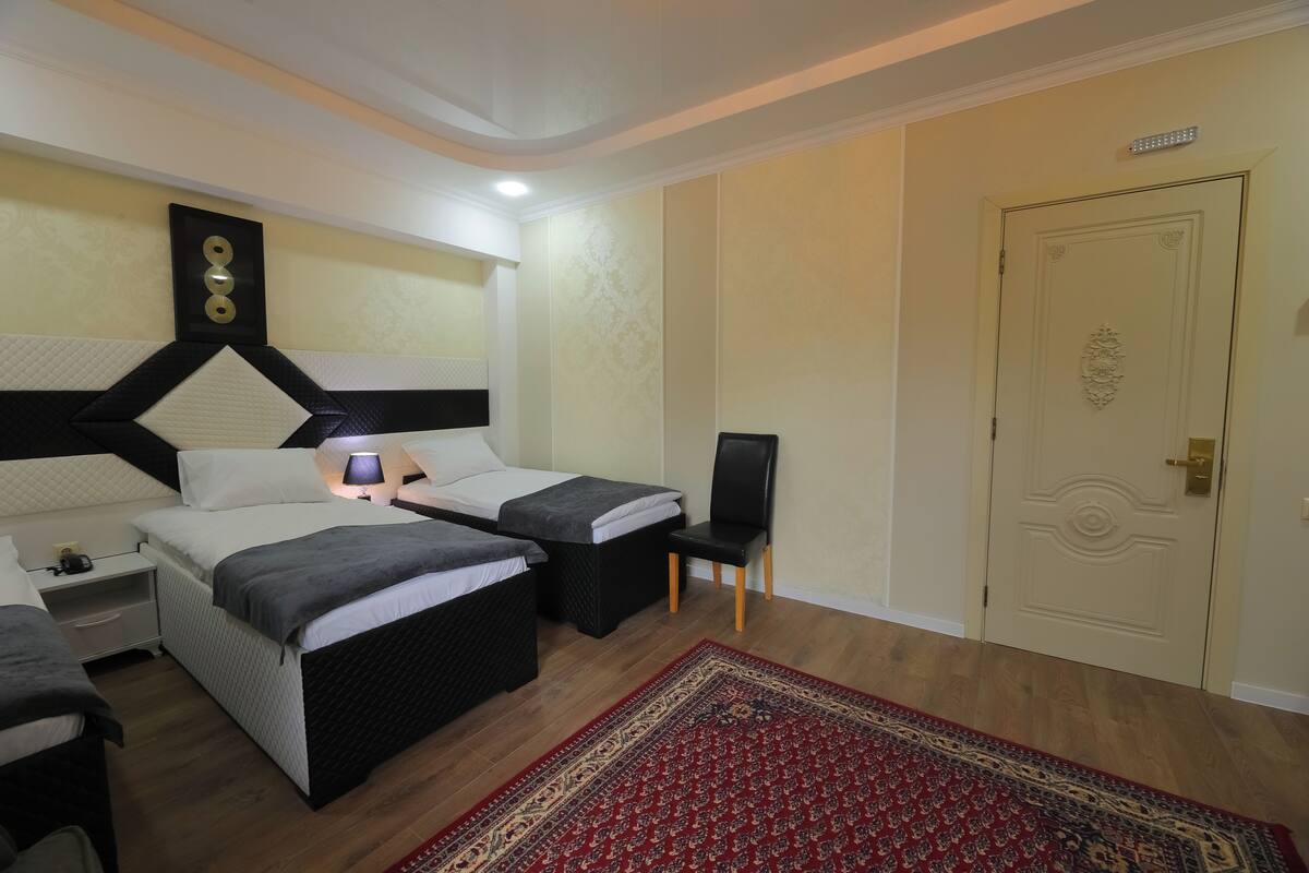 Ein Hotelzimmer mit zwei Betten, einem Nachttisch, einem Stuhl, einem roten Teppich mit Muster und einer Tür mit Zierdekor.