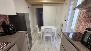 Una cocina moderna con armarios blancos, una mesa de comedor con sillas, horno empotrado y cafetera.