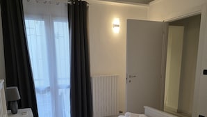 Habitación de hotel con una cama grande, una mesita de noche con lámpara, una ventana con cortinas, un radiador y un espejo.