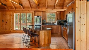 A wooden cabin kitchen with a central island, bar stools, and large windows. - The Epic Sunday River Getaway (Bethel)