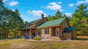 A log cabin with a green roof, large windows, and a porch with outdoor seating. - The Epic Sunday River Getaway (Bethel)