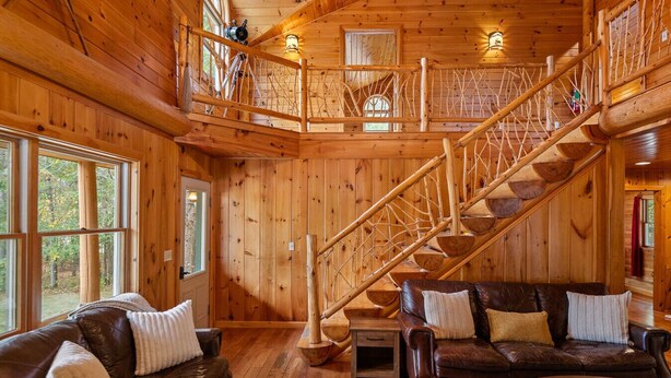 A wooden cabin interior with a loft bedroom, a staircase, and two leather sofas. - The Epic Sunday River Getaway (Bethel)