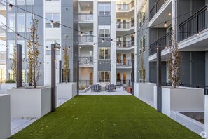 A modern apartment building with a central courtyard featuring artificial grass, outdoor seating, and string lights. - Luxury 2BR Steps from Railroad Park (Birmingham)