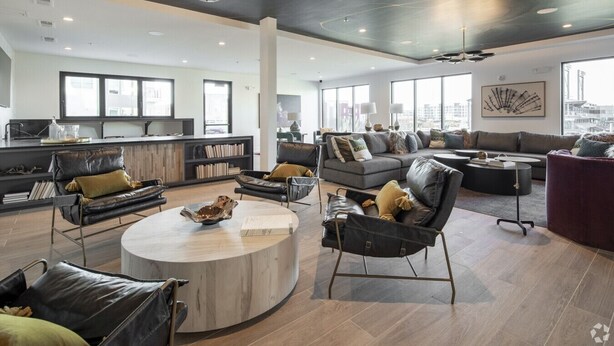 A spacious living area with a modern design, featuring leather sofas, a round coffee table, and a large window offering a city view. - Parkside Chic 2BR Near Regions Field + Park (Birmingham)
