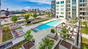 A rooftop pool area with lounge chairs and a swimming pool, surrounded by greenery and modern buildings.