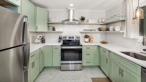 Une cuisine compacte avec des meubles de couleur vert clair, un réfrigérateur en acier inoxydable, un four encastré et un évier.