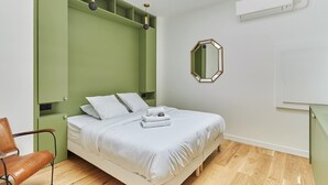 A bedroom with a bed, a green storage unit, a chair, a mirror, and an air conditioning unit. - Superb AC Loft 3 bdr - Paris Pere Lachaise (Paris)