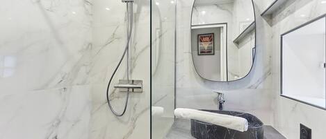 Une salle de bain moderne avec une douche à parois de verre, un mur recouvert de carreaux de marbre, un lavabo en marbre noir et un grand miroir.