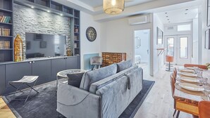 A modern living room with a grey sofa, a dining area with a wooden table set for four, and a kitchen with a stone backsplash and built-in shelves. - Superb AC Loft 3 bdr - Paris Pere Lachaise (Paris)
