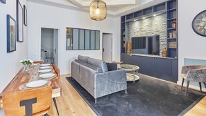 A modern living room with a sofa, dining table, and chairs. There is a fireplace, bookshelves, and a TV. - Superb AC Loft 3 bdr - Paris Pere Lachaise (Paris)