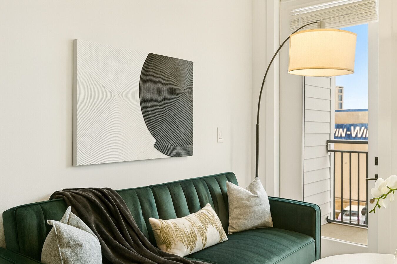 A green sofa with multiple cushions, a floor lamp, and a piece of abstract art on the wall.