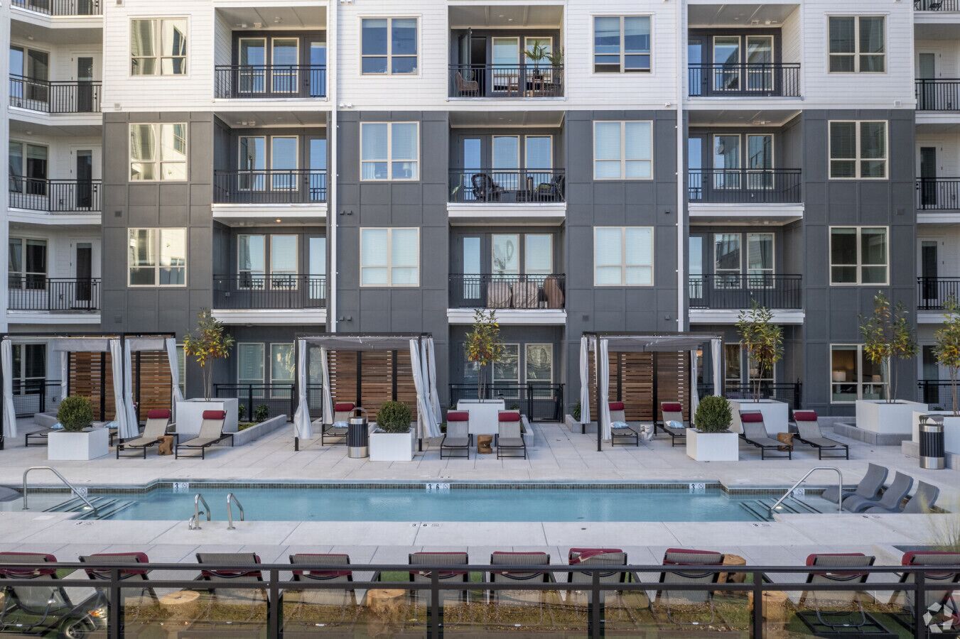 Un immeuble résidentiel à plusieurs étages doté d’une piscine, d’un espace extérieur aménagé et de balcons.