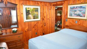 A wooden-paneled room with a bed, dresser, and two framed paintings.