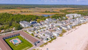 An aerial view of a coastal resort with multiple buildings, a swimming pool, and a beach.