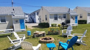 A backyard with white and blue Adirondack chairs, a fire pit, and a small table.