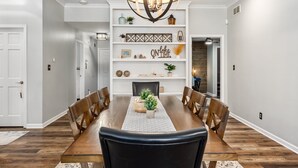 Un comedor con una mesa de madera, sillas, una araña y estantes con objetos decorativos.