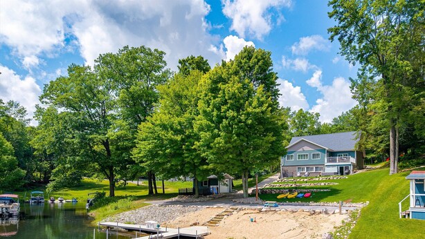 Una propiedad frente al lago con un muelle, una casa con balcón y una zona verde con kayaks.