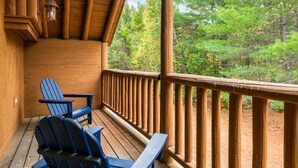Een houten terras met twee Adirondack-stoelen en een lantaarn.