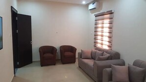 A living room with a sofa, two armchairs, a closed door, and a window with blinds.
