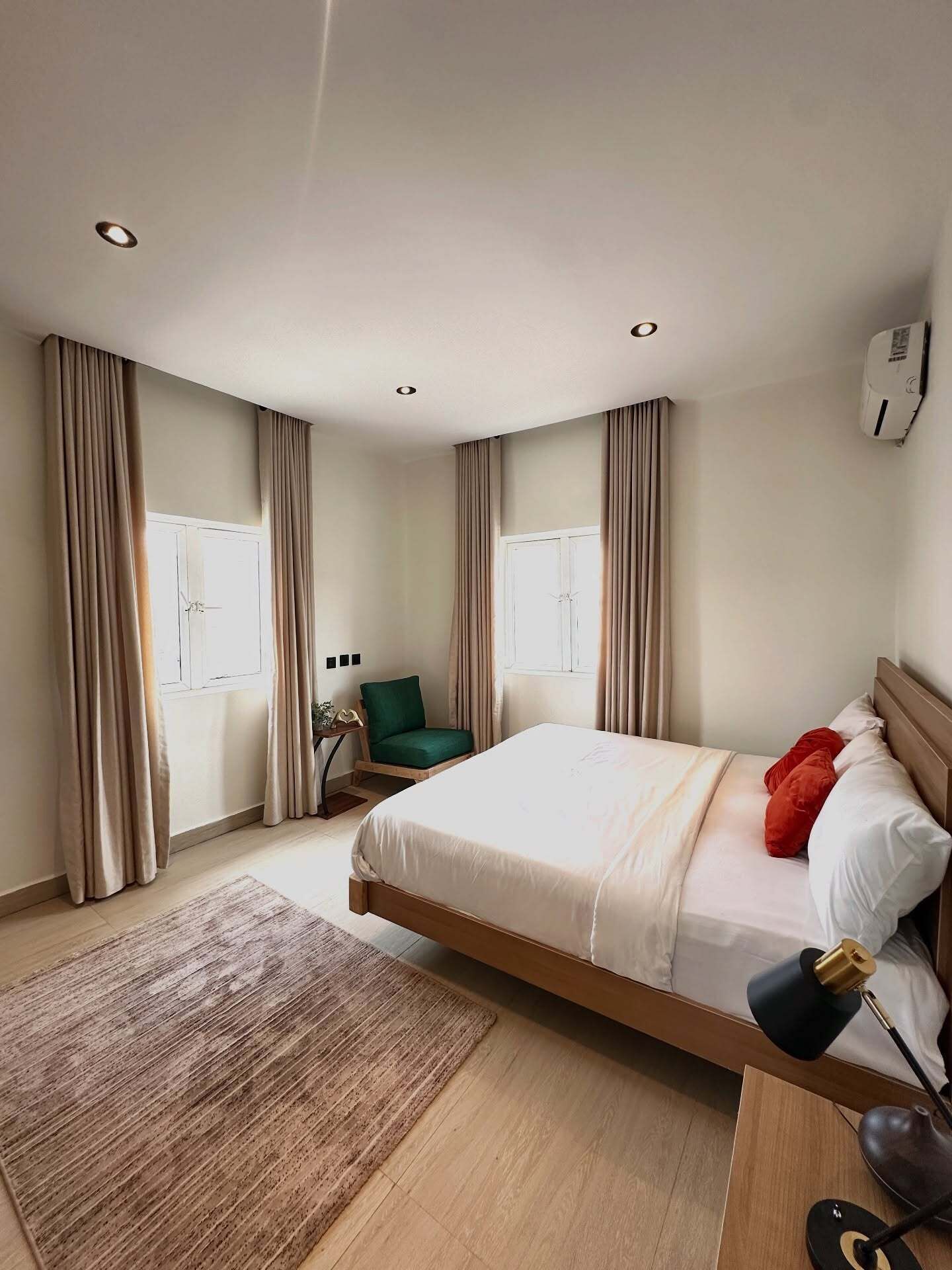 A modern hotel room with a large bed, a desk, a chair, and an air conditioning unit.