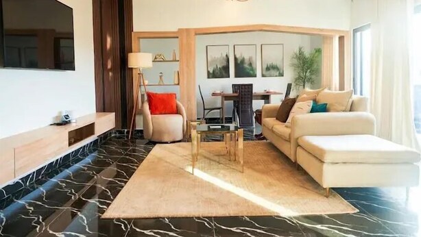 A modern living room with a flat-screen TV, a sofa, a coffee table, and a chandelier.
