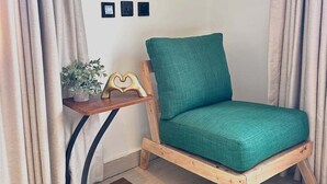 A corner room with a wooden chair, a small table with a plant, and a wall-mounted light switch.