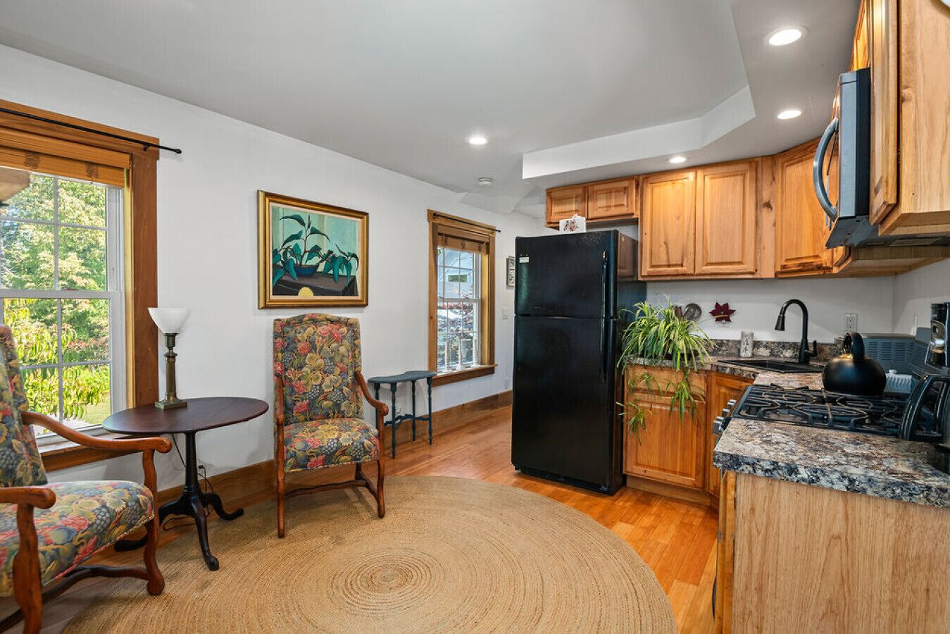 Una cocina con armarios de madera, un refrigerador negro, una estufa y un comedor con una silla y mesa.