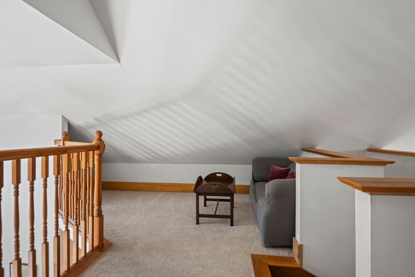 Un dormitorio tipo loft con techo inclinado, una escalera de madera, un sofá gris y una pequeña mesa de madera.
