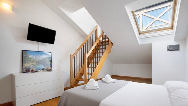 Une chambre à coucher avec un lit, un téléviseur fixé au mur, un tableau, un escalier en bois et une lucarne.
