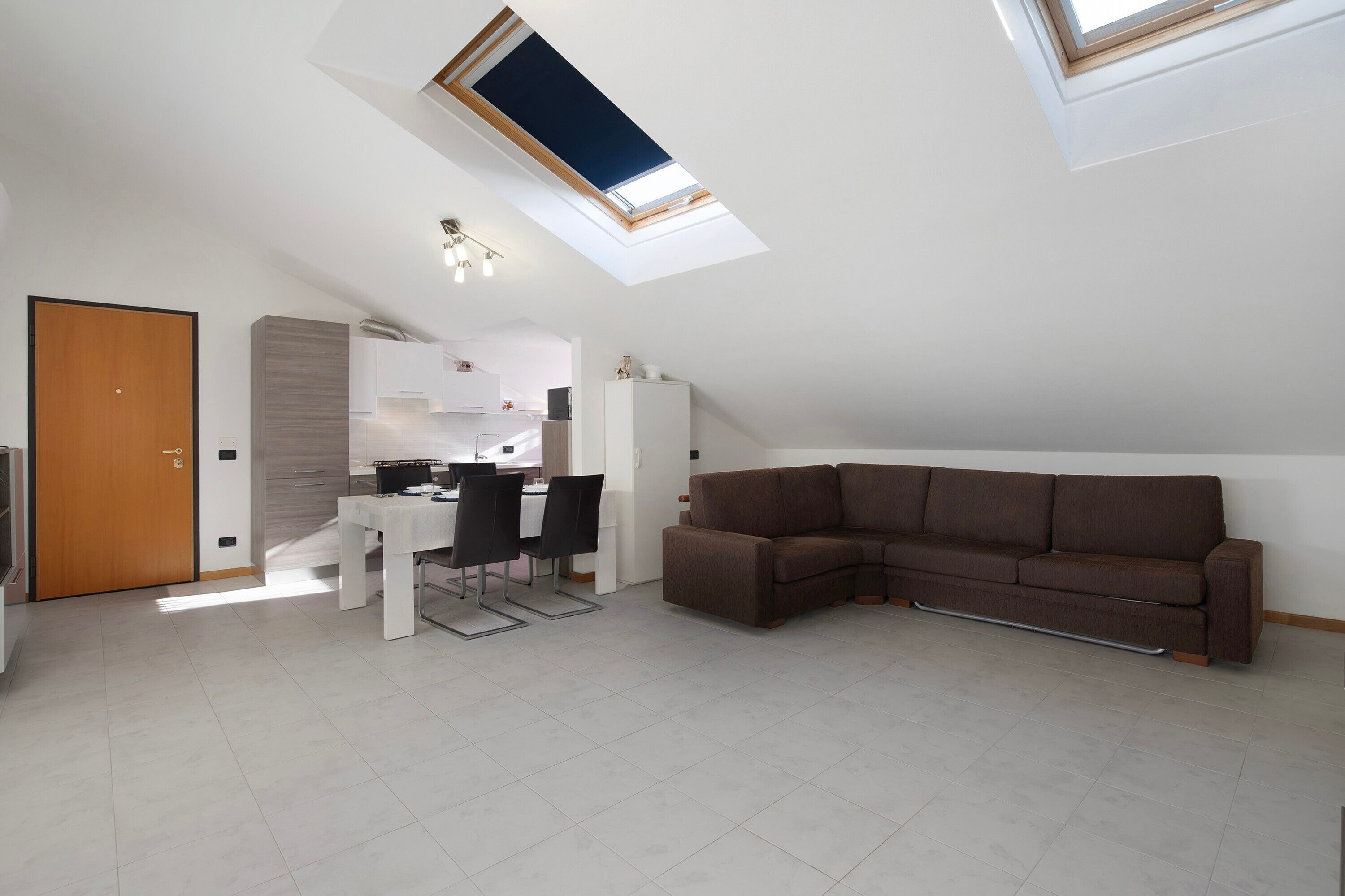A modern loft apartment with a skylight, a dining area, a sofa, and a kitchen.