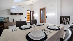 Une salle à manger avec une table dressée pour quatre personnes, un coin cuisine doté d’une étagère intégrée et une vue sur l’extérieur par une fenêtre.