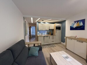 A compact living space with a sofa, a dining table, a kitchenette, and a painting on the wall.
