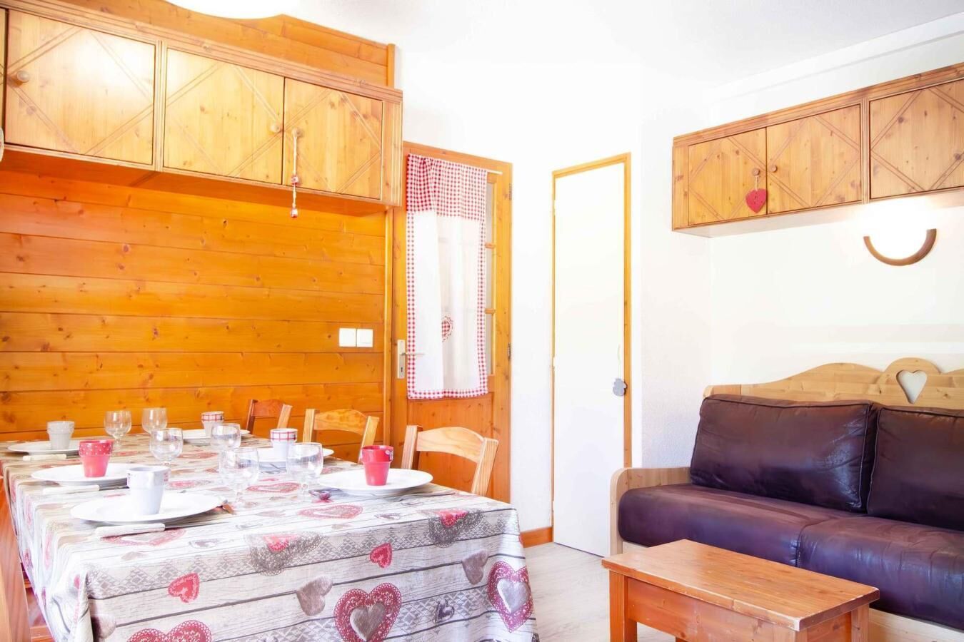 Ein gemütliches Zimmer mit einem Holzespeisetisch, gedeckt für vier Personen, einer Ledersofa und Holzschränken.