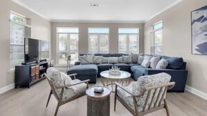 Un salon moderne avec un canapé d’angle, un meuble pour la télévision, des fauteuils en osier et une table basse ronde.
