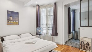 A bedroom with a bed, a window with curtains, a radiator, a fan, and a poster on the wall. - Champs de Mars - Ecole Militaire 1bdr by B'Your Home (Paris)