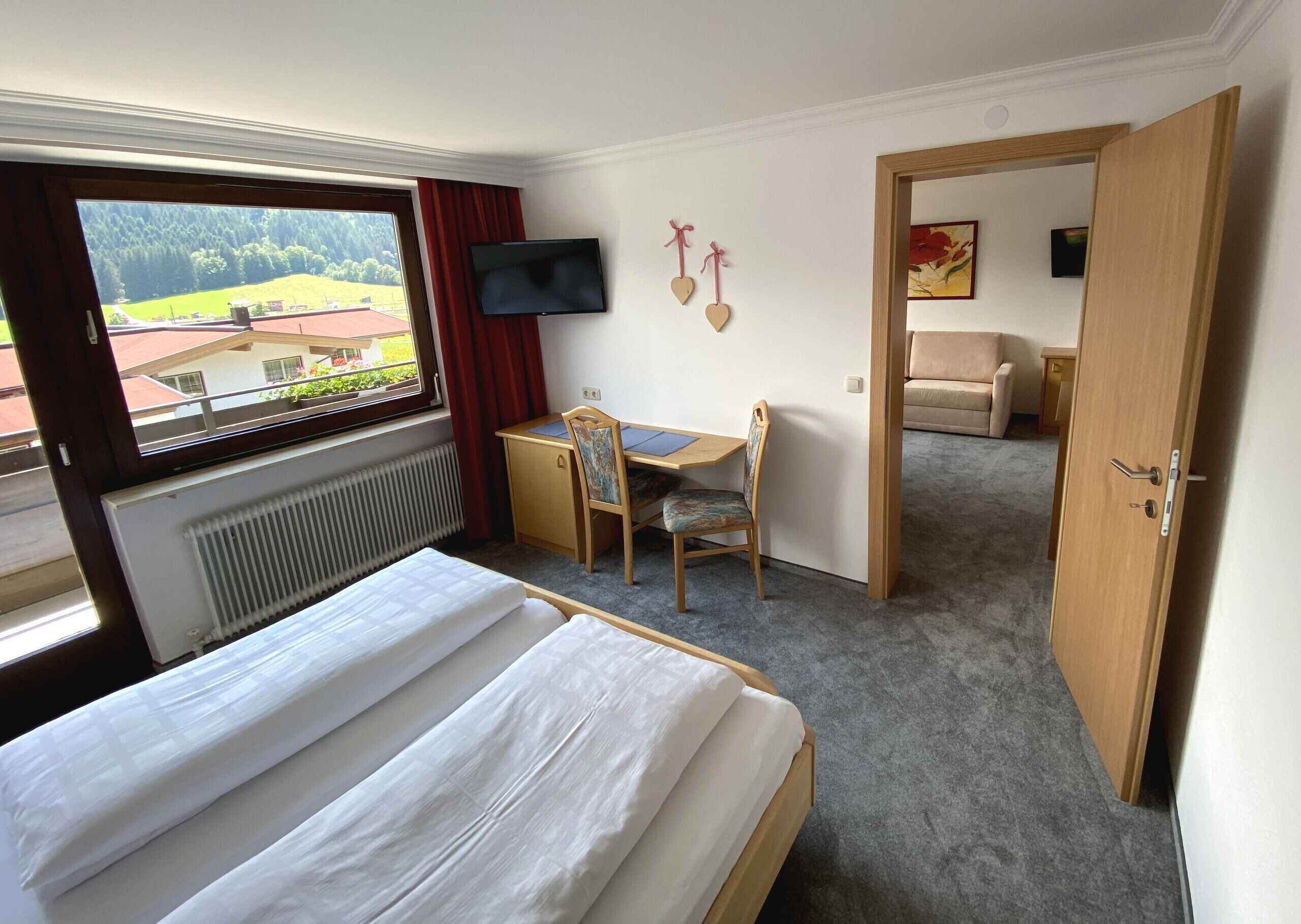 A hotel room with a bed, a desk with a chair, a TV, and a view of the outdoors.